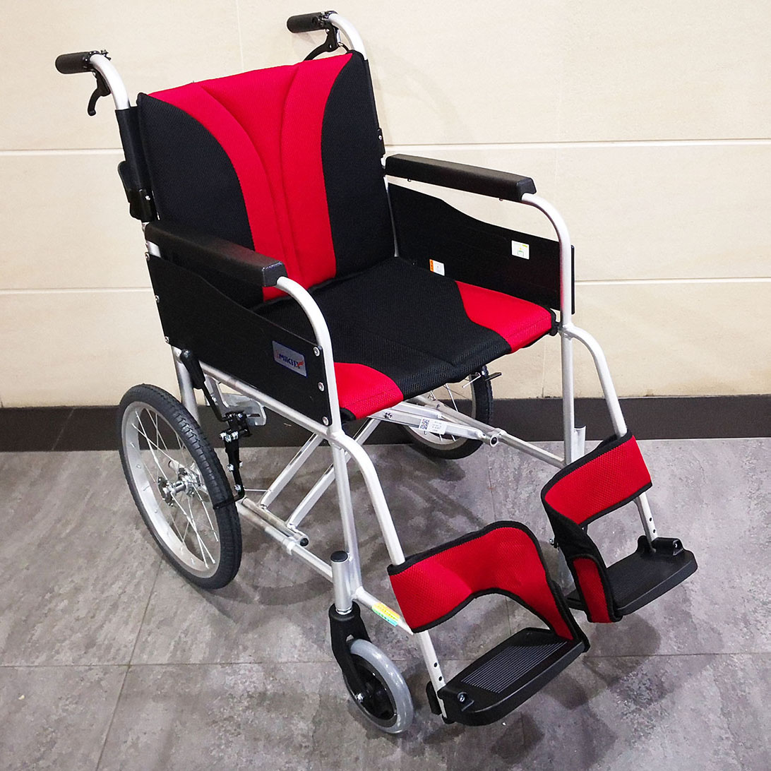 輪椅王 紅黑相間的手動輪椅，配有金屬框架、軟墊座椅和腳踏板，放置在瓷磚地板上，靠著淺色牆壁。